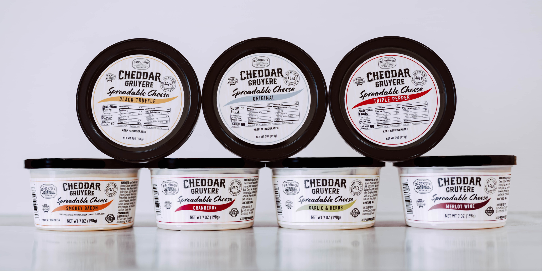Row of Cheddar Gruyere Spreadable Cheese containers on a white background